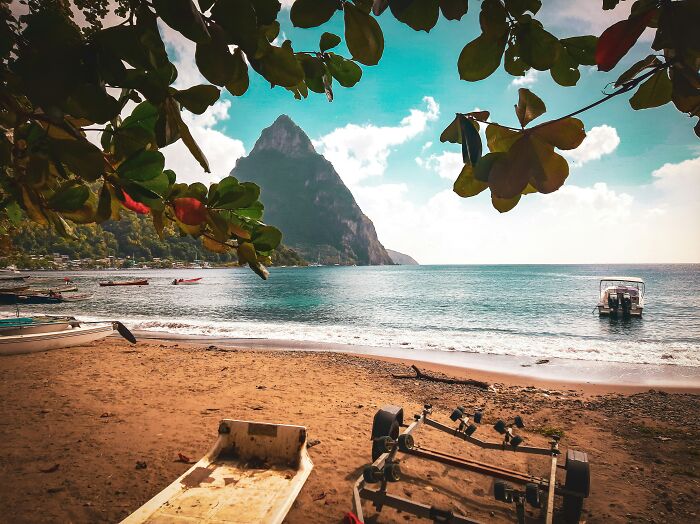Tropical beach with clear water, boats, and a mountain peak framed by leaves, showcasing wonders that prove the world is full of magic.