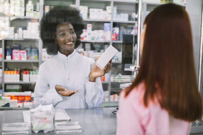 Pharmacist sharing a product detail with a customer behind the counter, revealing a company secret in a retail setting.