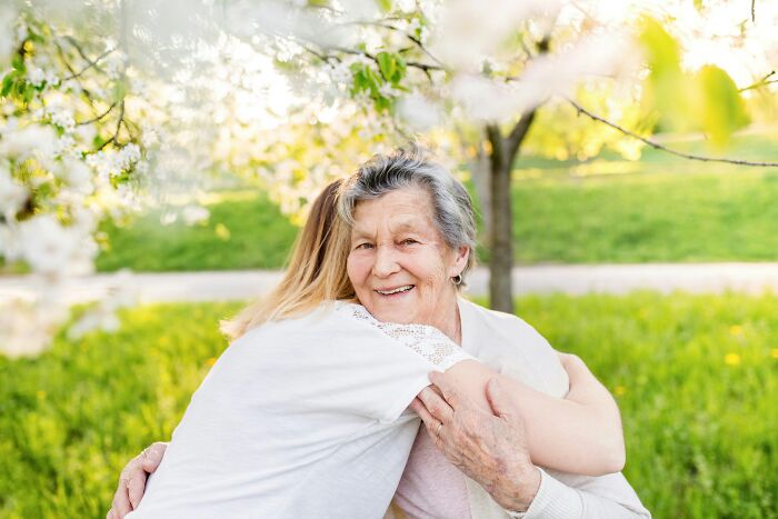 Elderly woman and younger person hugging under blooming tree, reflecting harsh life gives you lemons advice.