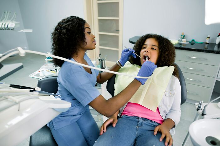 Dentist examining young girl’s teeth in clinic, illustrating hilariously bad names that make people question parents’ choices.