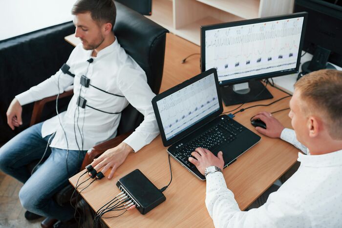 Man undergoing a polygraph test while technician monitors results on laptop and desktop screens showing placebo effect data.