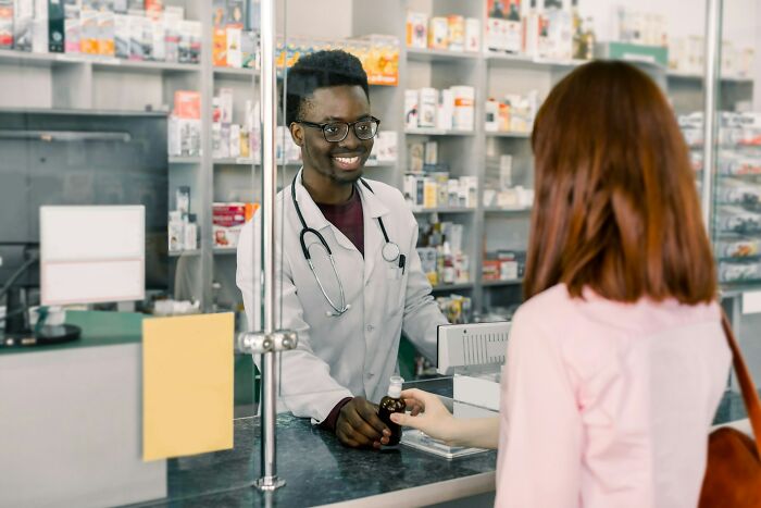 Pharmacist behind counter handing medicine to customer in pharmacy revealing industry secrets behind closed doors.