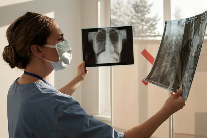 Doctor in scrubs and mask examining unusual X-ray scans as part of weird and unhinged finds shared by medical professionals.