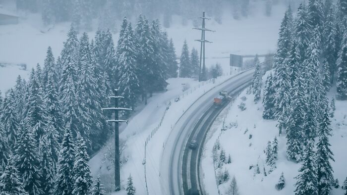 Snow-covered road winding through dense forest with vehicles, showing shocking real-life winter driving experiences.
