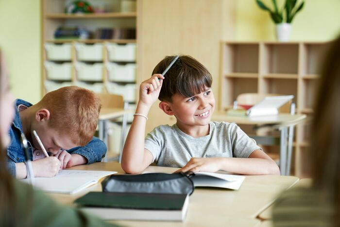 Two young boys sitting at a classroom desk, one smiling and holding a pencil, illustrating boomer opinions in school.