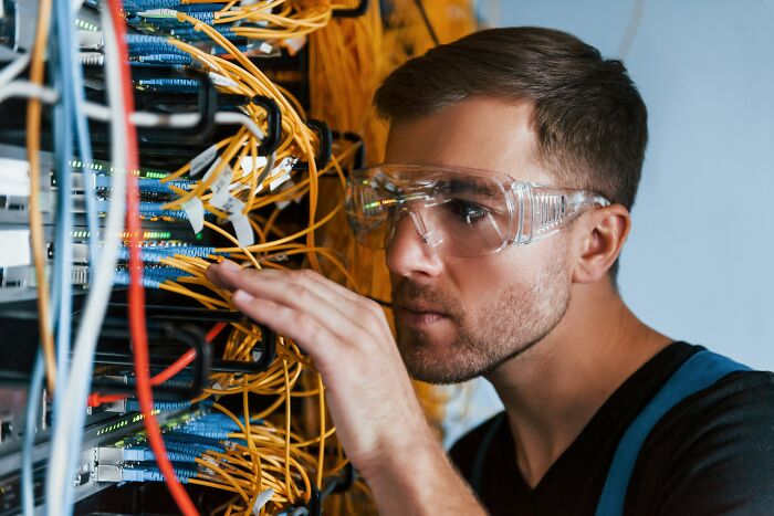 Man wearing safety glasses working with tangled network cables, illustrating weirdest ways to earn quick money.