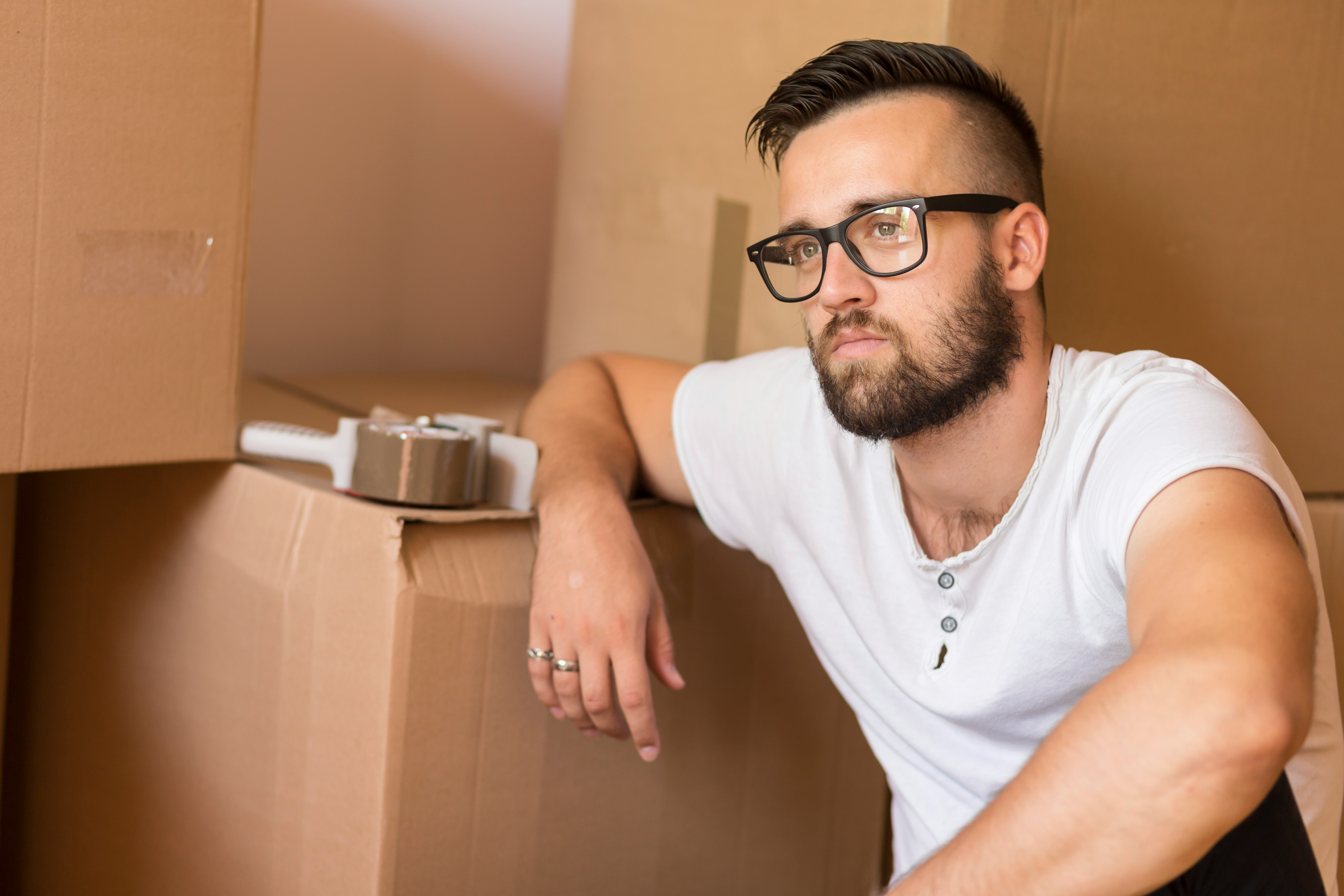 Man with glasses and beard leaning on packed cardboard boxes reflecting on petty revenge years later Man with glasses and beard leaning on packed cardboard boxes reflecting on petty revenge years later