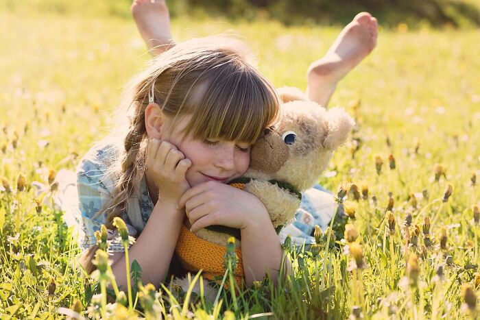 Young girl lying in a field hugging a teddy bear, illustrating hilariously bad names that had people questioning parents' choices.