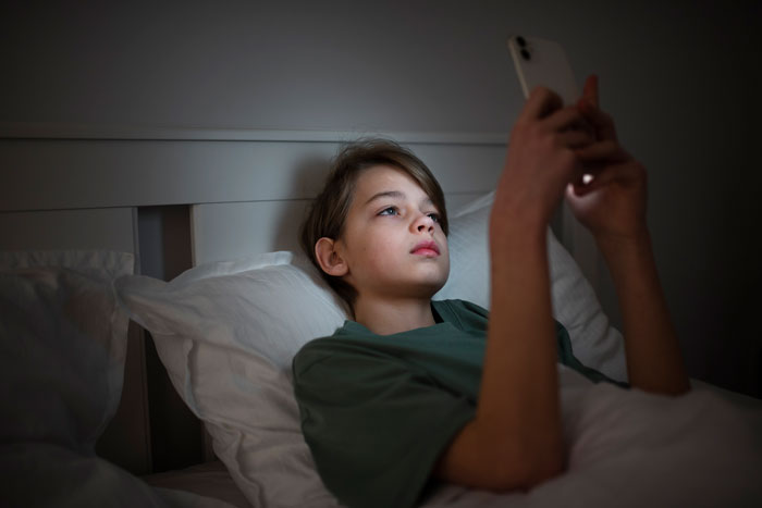 Young boy in bed using smartphone late at night, highlighting monitoring and demands for an open door by 11YO son.