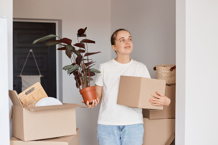Young man holding a box and plant, surrounded by moving boxes, reflecting life changes after ruining things with partner