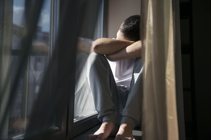 Man sitting by a window with head resting on arms, reflecting on how life turned upside down after ruining things with partner.