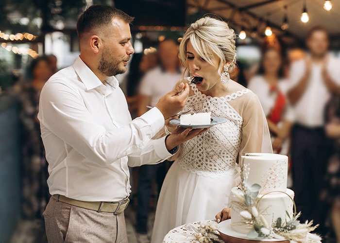 Groom feeding bride cake at wedding reception, moments before a cake smash incident with a fork occurs. Groom feeding bride cake at wedding reception, moments before a cake smash incident with a fork occurs.