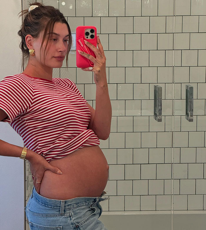 Hailey Bieber in a striped shirt taking a mirror selfie, relating to Justin Bieber's controversial Mother's Day post.