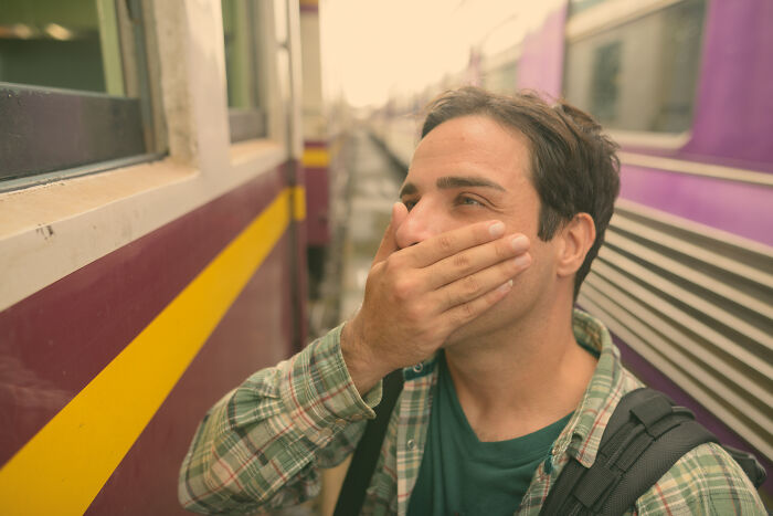 A man covering his mouth in shock while standing between two trains, experiencing a shocking moment.