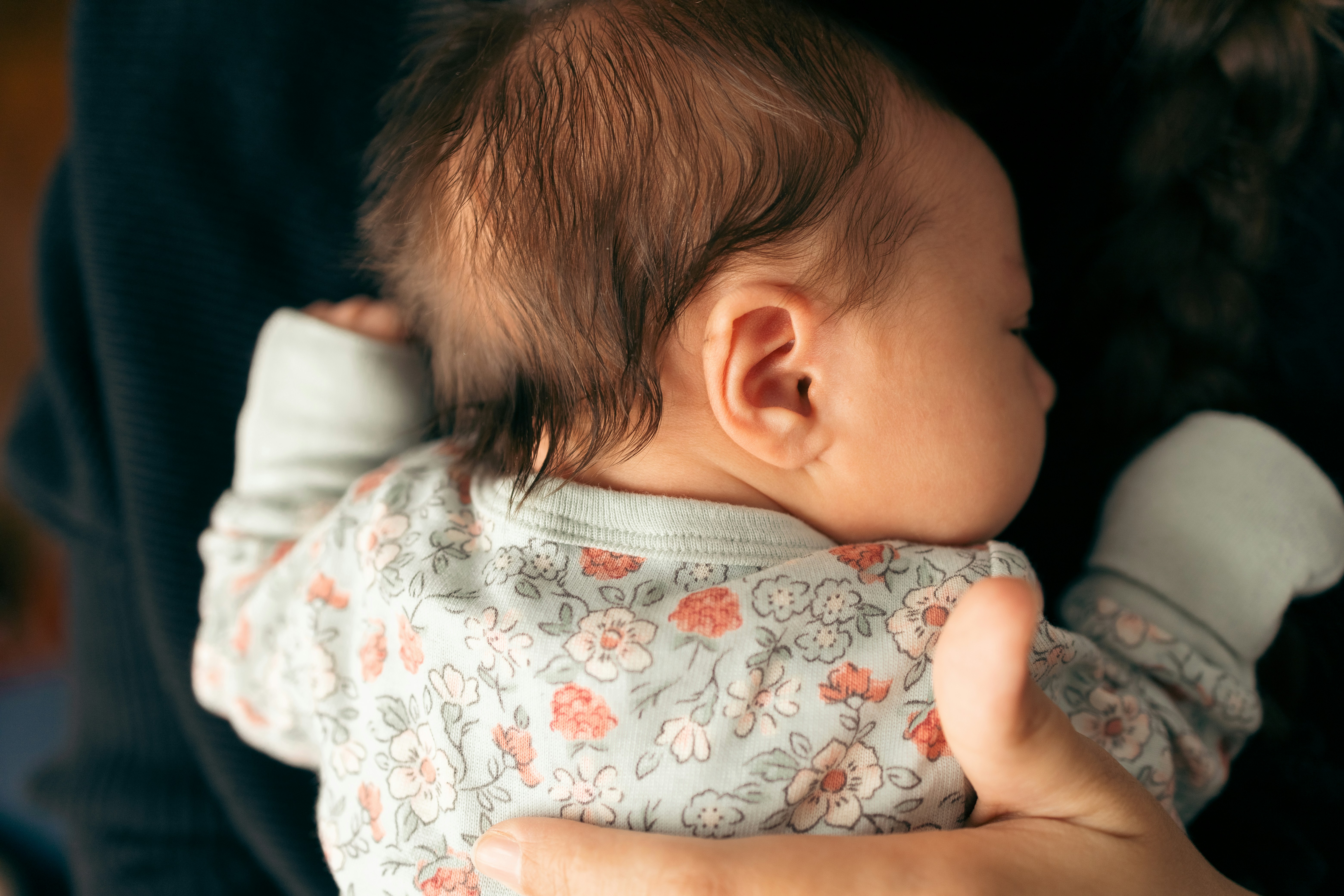 Close-up of a baby in floral clothes being gently held, relating to keeping son away from grandmother after fed custard.
