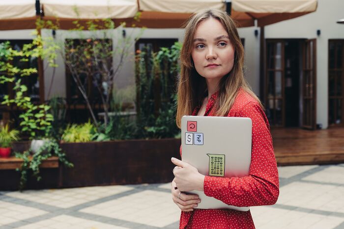 Young woman in red dress holding laptop outdoors, symbolizing childhood habits and attention-seeking red flags.