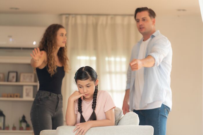 Parents arguing and pointing at a sad child, illustrating childhood habits as red flags in behavior and attention-seeking.
