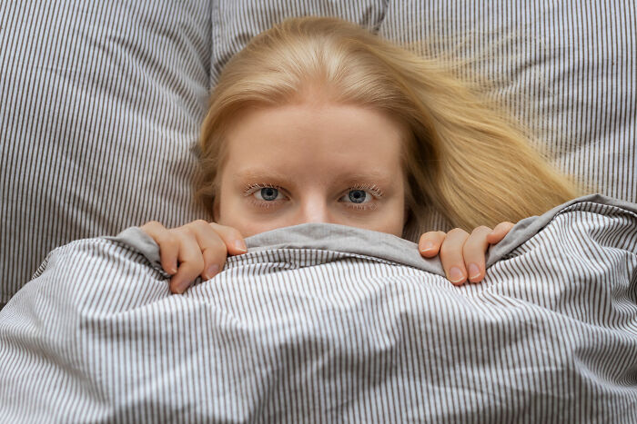 Young woman hiding under striped blanket, illustrating childhood habits as red flags and attention-seeking behaviors.