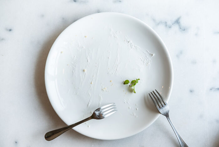 Empty white plate with two forks on a marble table, symbolizing childhood habits that are red flags and attention-seeking behavior.