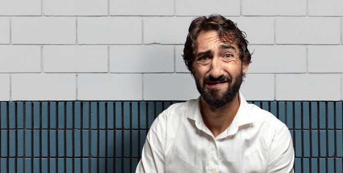 Man with confused expression sitting against blue and white tiled wall representing childhood habits as red flags concept.