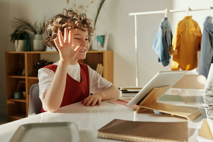 Child with curly hair raising hand during online learning, illustrating childhood habits and red flags awareness.