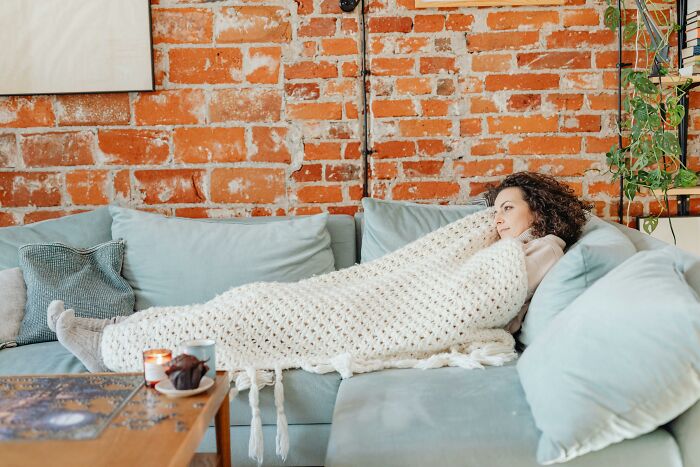 Woman wrapped in blanket lying on a sofa, reflecting on childhood habits as potential red flags in behavior.