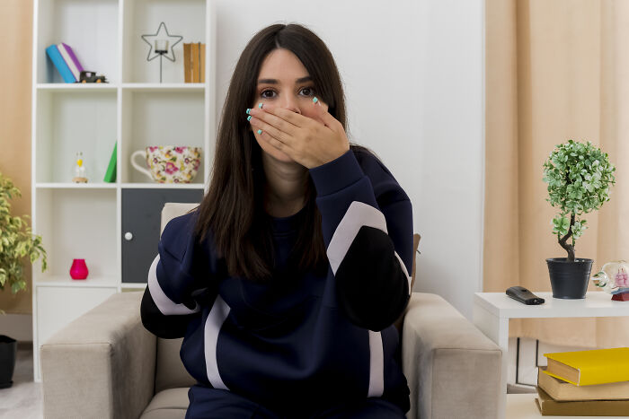 Young woman covering her mouth sitting on a couch, illustrating childhood habits that reveal red flags.