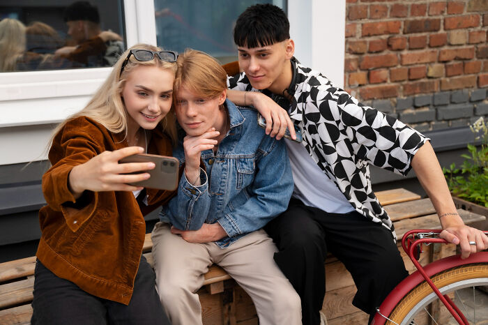 Three teenagers sitting on a bench taking a selfie outdoors, illustrating attention-seeking childhood habits as red flags.