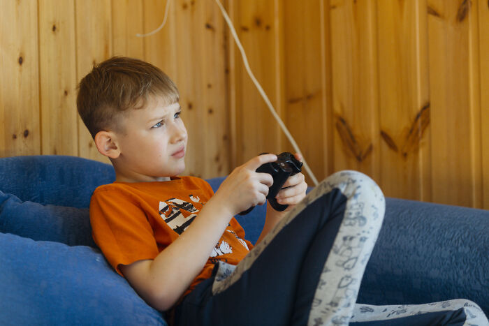 Young boy sitting on a couch playing video games, illustrating childhood habits that can be red flags in behavior.