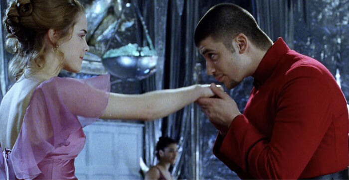 Actor who played Viktor Krum in Harry Potter seen in a scene at the Yule Ball wearing a red outfit and kissing a woman's hand.