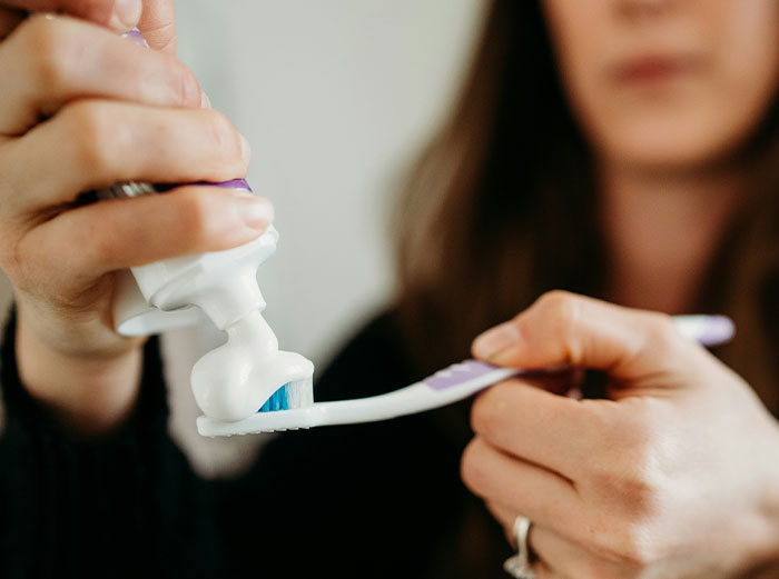 Person squeezing toothpaste onto a toothbrush, symbolizing dental care advice about healthy foods to skip.