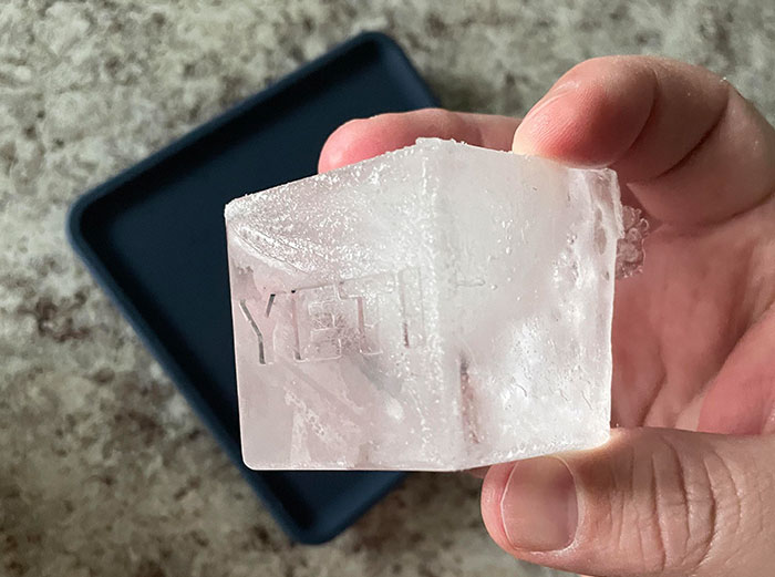 Hand holding a clear square ice cube from a Yeti tray, related to healthy foods dentists and doctors suggest skipping.