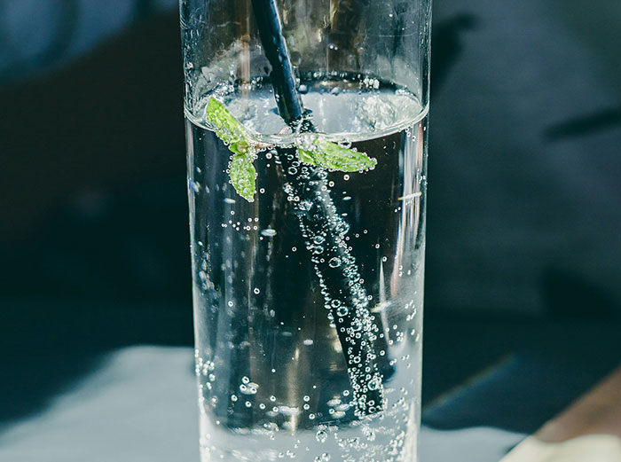 Glass of sparkling water with a mint leaf and black straw, representing healthy foods to skip according to dentists and doctors.