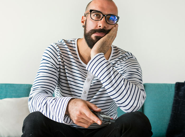 Man with glasses and beard wearing striped shirt, sitting and appearing thoughtful, illustrating employee figures out work strategy. Man with glasses and beard wearing striped shirt, sitting and appearing thoughtful, illustrating employee figures out work strategy.