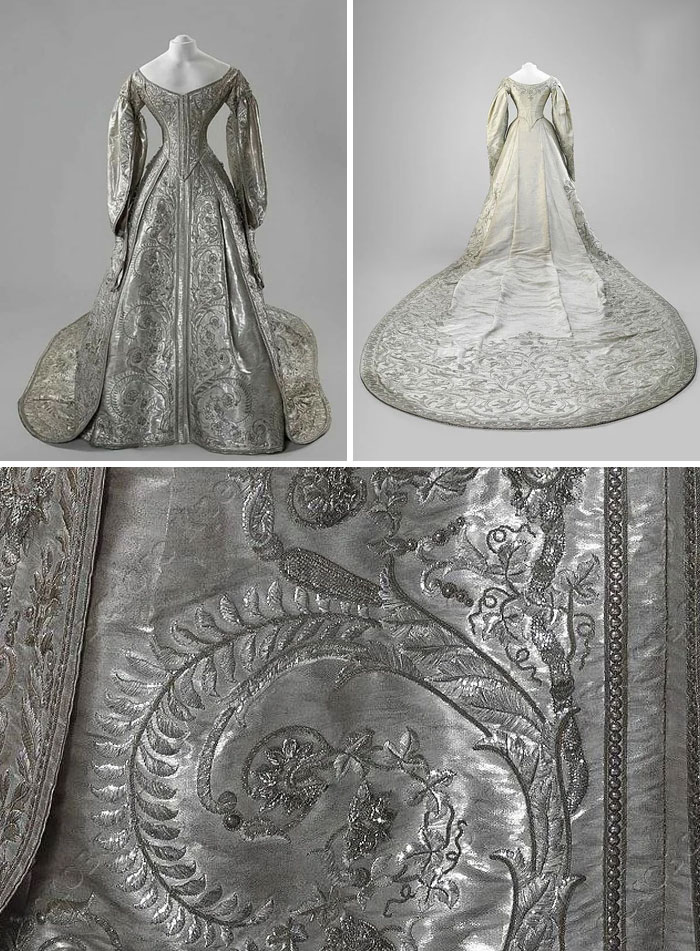 Silver embroidered historical gown with long train and detailed floral patterns, showcasing centuries of fashion craftsmanship.