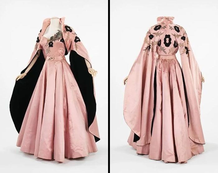 Vintage pink satin gown with embroidered black floral details and matching cape, showcasing centuries of fashion history.