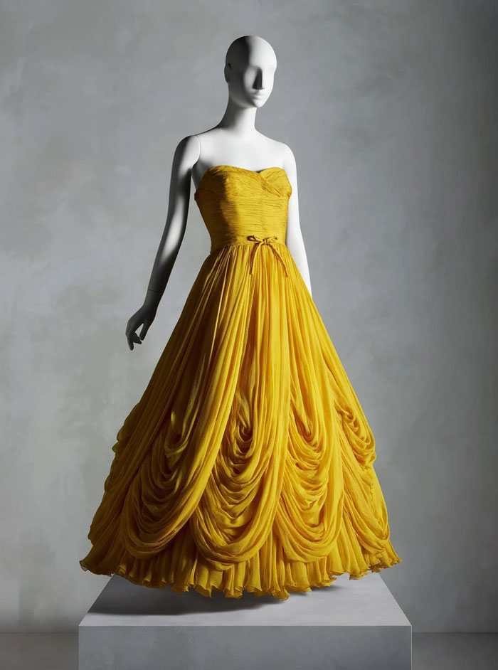 Yellow vintage gown on a mannequin, showcasing centuries of fashion with intricate draping and elegant design details.