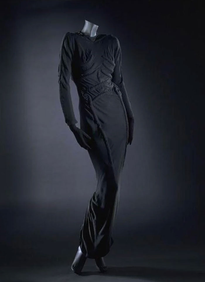 Black fitted vintage dress on a mannequin, showcasing centuries of fashion evolution in a dark studio setting.