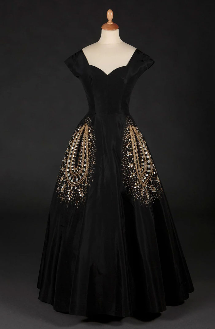 Classic black evening gown with intricate gold embroidery, showcasing historical fashion trends from a few centuries ago.