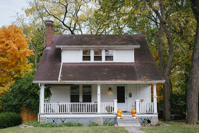 Cozy suburban house with autumn trees, pumpkins on porch, representing nostalgic Gen X lifestyle and home comforts.