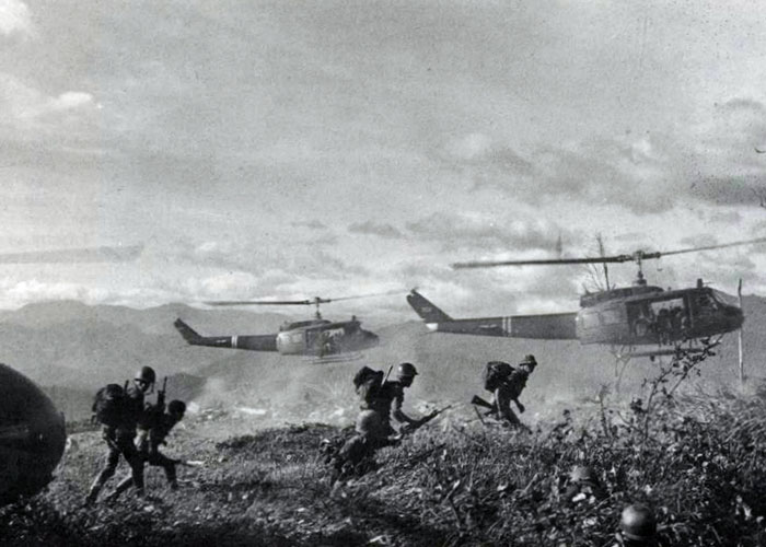 Black and white image of soldiers disembarking from helicopters during a historical military operation in a rugged landscape.