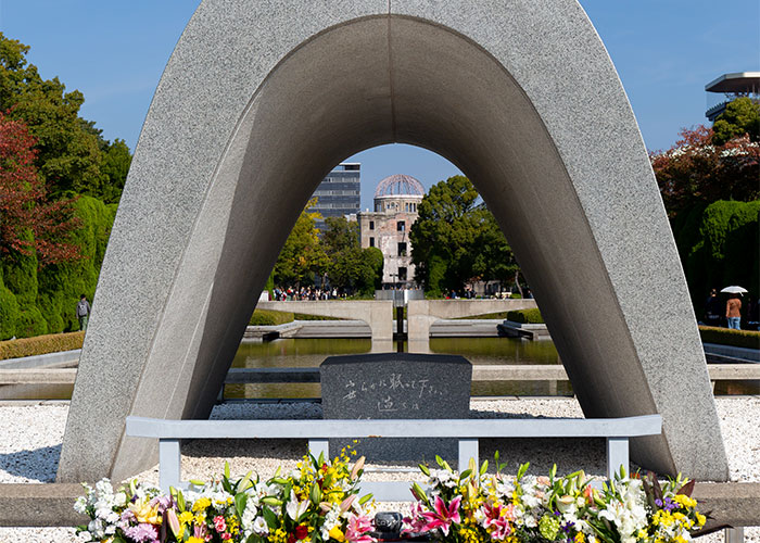Hiroshima Peace Memorial under arch monument with flowers in foreground, a historical site that draws continuous research interest.