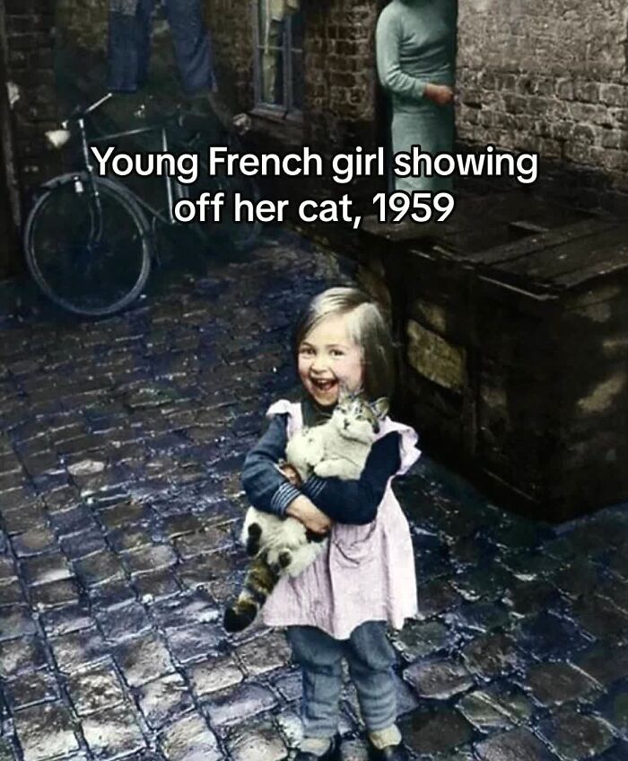 Young French girl happily holding her cat on a cobblestone street in 1959, a monumental life moment frozen in time.