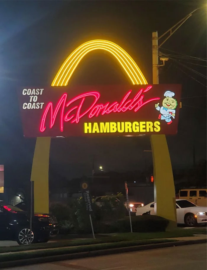 Vintage McDonald's neon sign with classic golden arches and retro mascot at night, showing how things used to look.