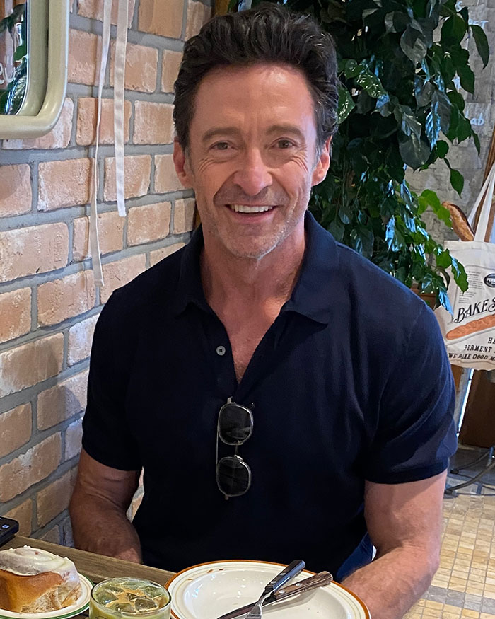 Hugh Jackman smiling indoors at a table, childhood friend breaks silence on actor's divorce and aging wife rumors. Hugh Jackman smiling indoors at a table, childhood friend breaks silence on actor's divorce and aging wife rumors.