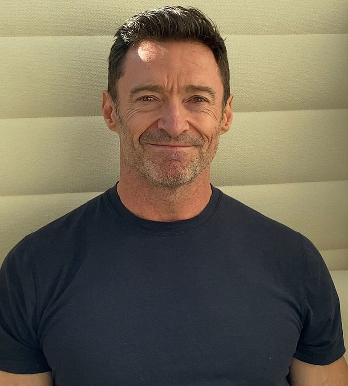Hugh Jackman smiling in a black t-shirt, highlighting his long history with Sutton Foster amid divorce news.