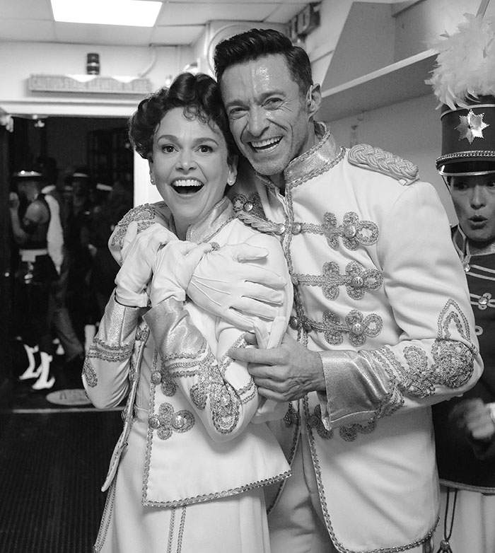 Hugh Jackman and Sutton Foster smiling backstage in matching ornate costumes during a theatrical performance.