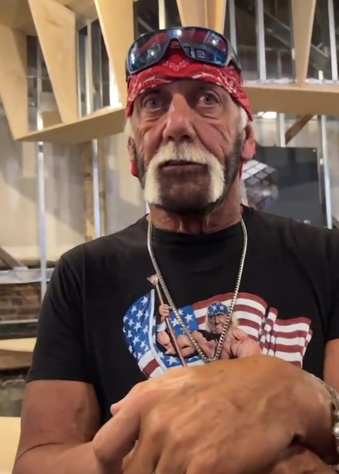 Hulk Hogan wearing a bandana and sunglasses on head showing a new look with intense eyes at 71 in an indoor setting.