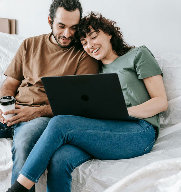 Couple sitting on couch looking at laptop, woman considering ending 24-year marriage over paternity test demand. Couple sitting on couch looking at laptop, woman considering ending 24-year marriage over paternity test demand.
