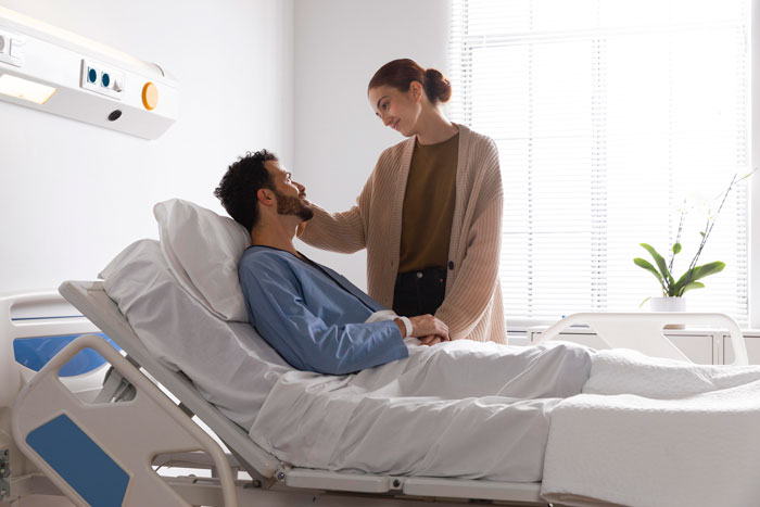 Man in hospital bed with woman comforting him, illustrating a sensitive moment related to telling kids about their dad's passing.